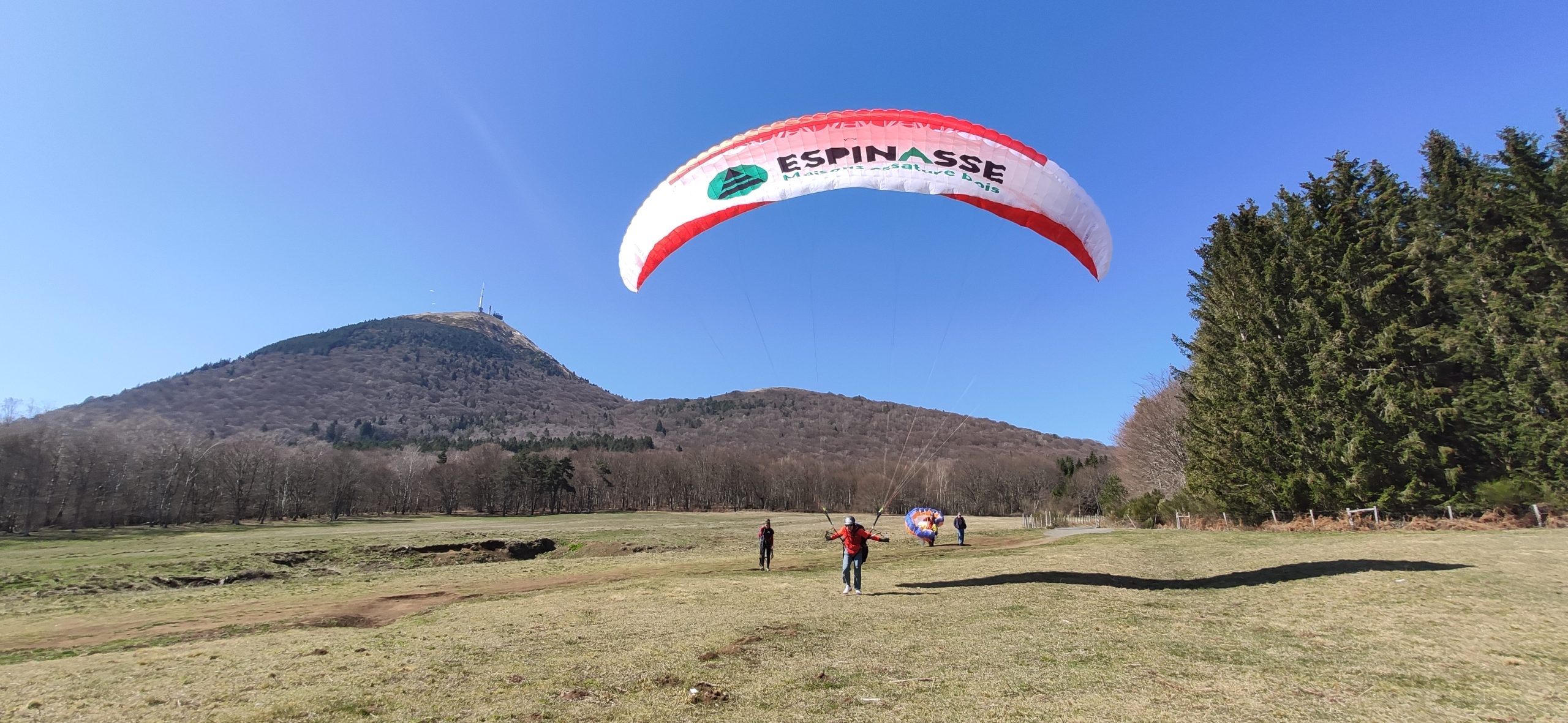 Atterrissage d'un parapente biplace au pied du Puy de Dôme, près de la gare du Panoramique des Dômes